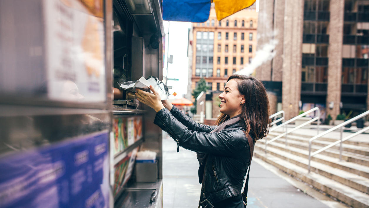Food-Trends 2016: Street Food, Meat Markets und regionale Produkte waren angesagt A beautiful Caucasian adult woman buys some lunch from a New York city food cart, a smile on her face. She wears modern stylish clothing with darker and black colors. Horizontal image with copy space.