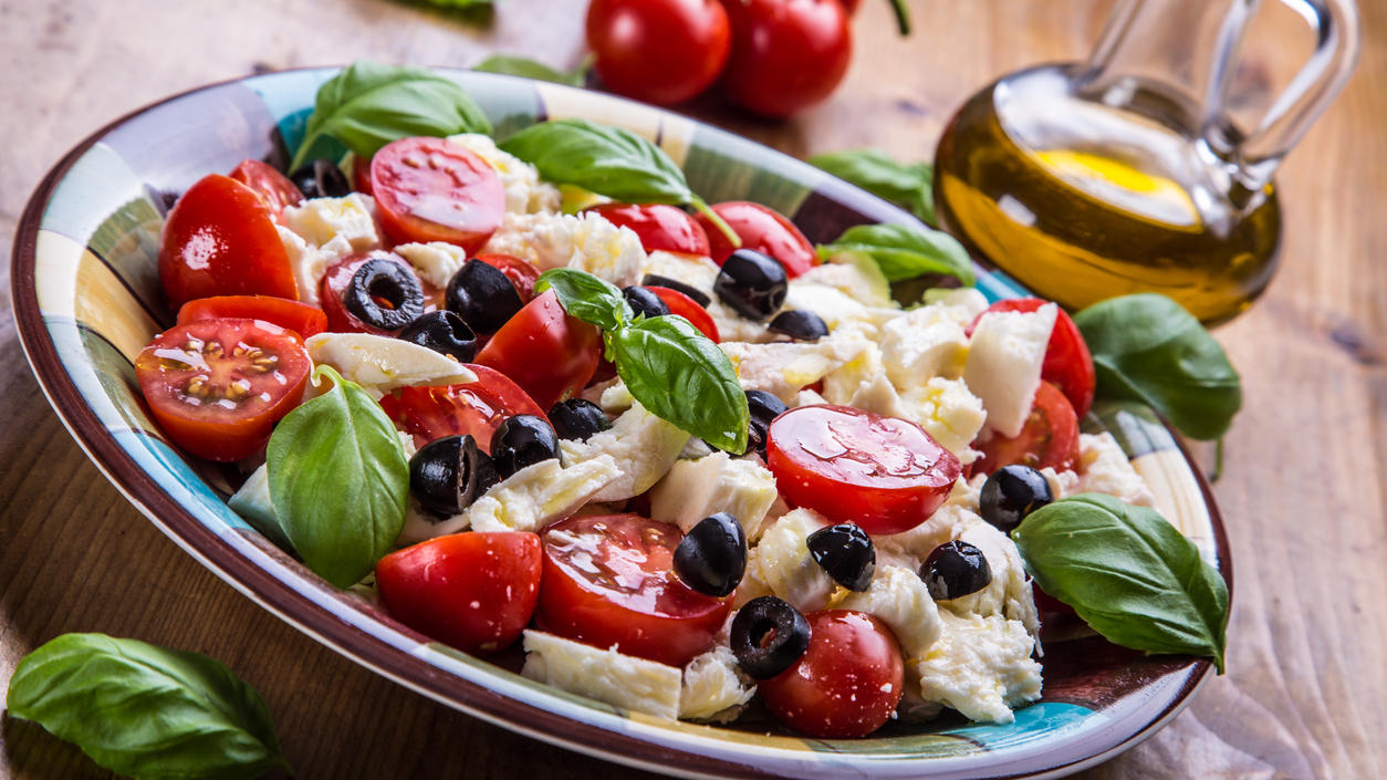 Mittelmeerdiät - laut Harvard-Studie am effektivsten beim Abnehmen Caprese. Caprese salad. Italian salad. Mediterranean salad. Italian cuisine. Mediterranean cuisine. Tomato mozzarella basil leaves black olives and olive oil on wooden table. Recipe - Ingredients