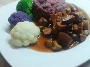 Seitan-Pilz-Gulasch an lila Kartoffelbrei mit orangen Tupfen und bunten Röschen - Rezept