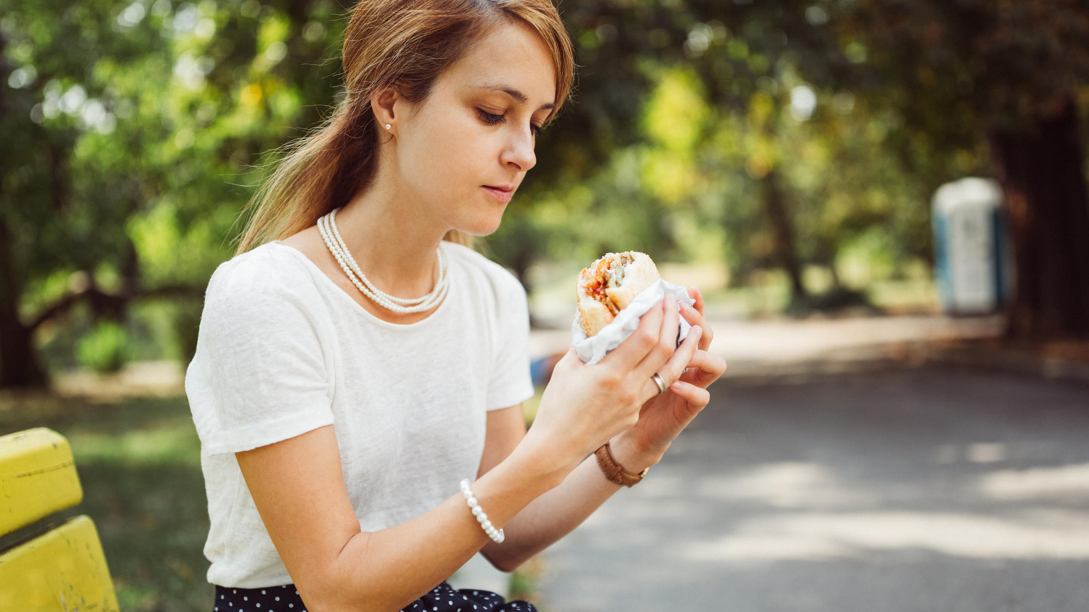 Studie warnt: Zu viel Fast Food erhöht das Risiko für Depressionen Frau ist Burger alleine im Park.