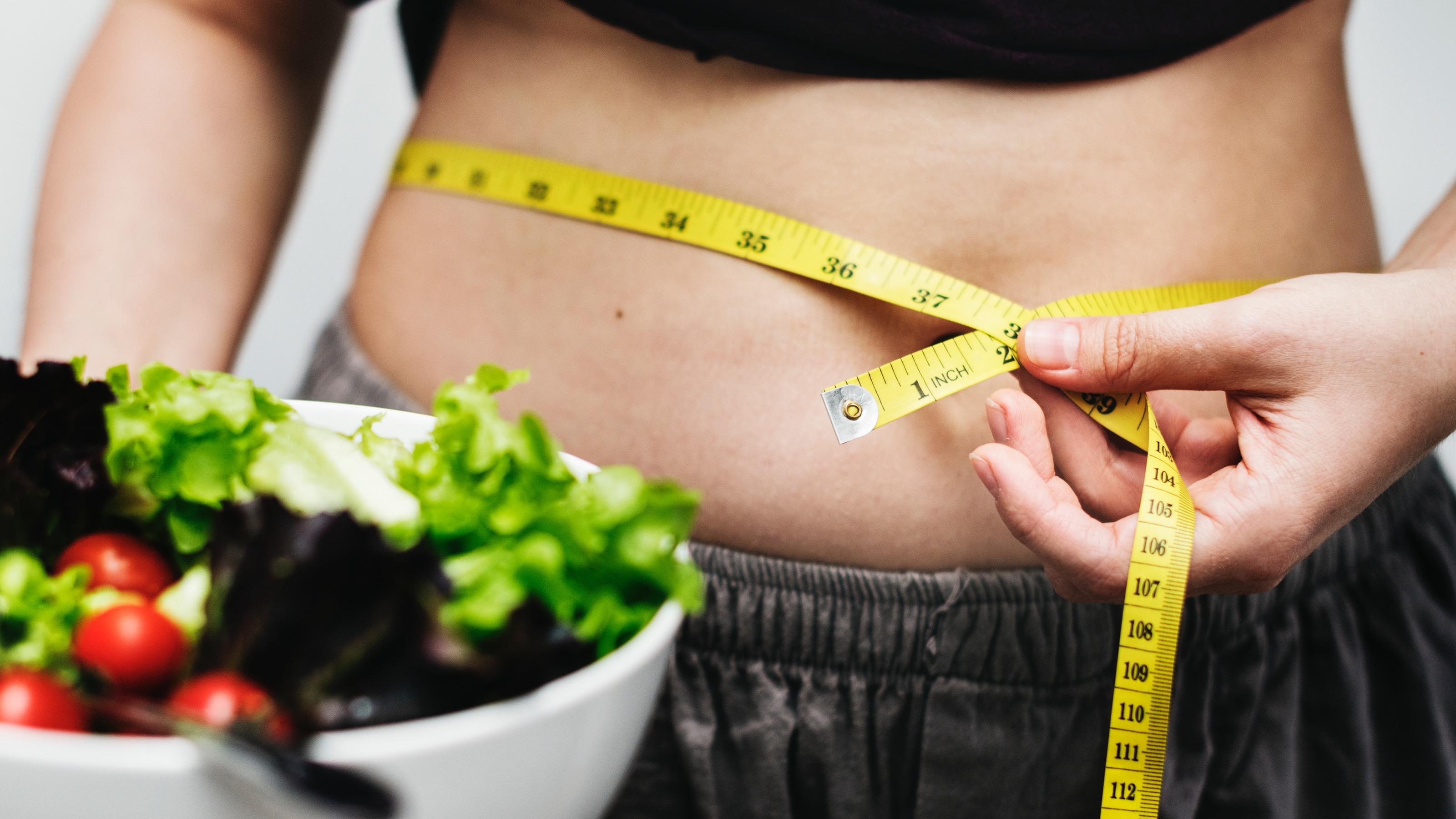 Ist das die erste Diät, die wirklich funktioniert? Frau mit Salat und Maßband um den Bauch