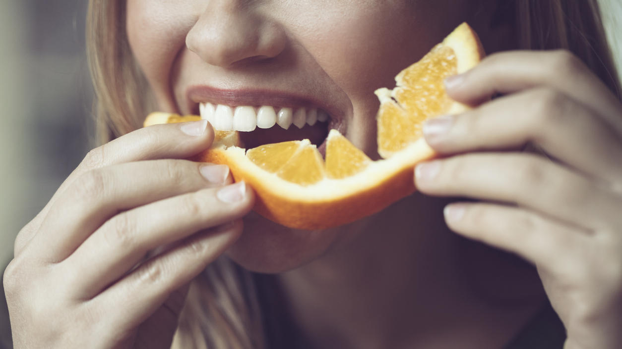 Verursacht vegane Ernährung schlechte Zähne? Frau isst Orange