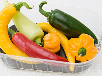 Chili & Co: Wofür Schärfe so alles gut ist Plastikschachtel mit verschiedenen Sorten von Chilischoten und Peperoni vor weißem Hintergrund.Plasticbox with different kind of chillies and peppers and white background.