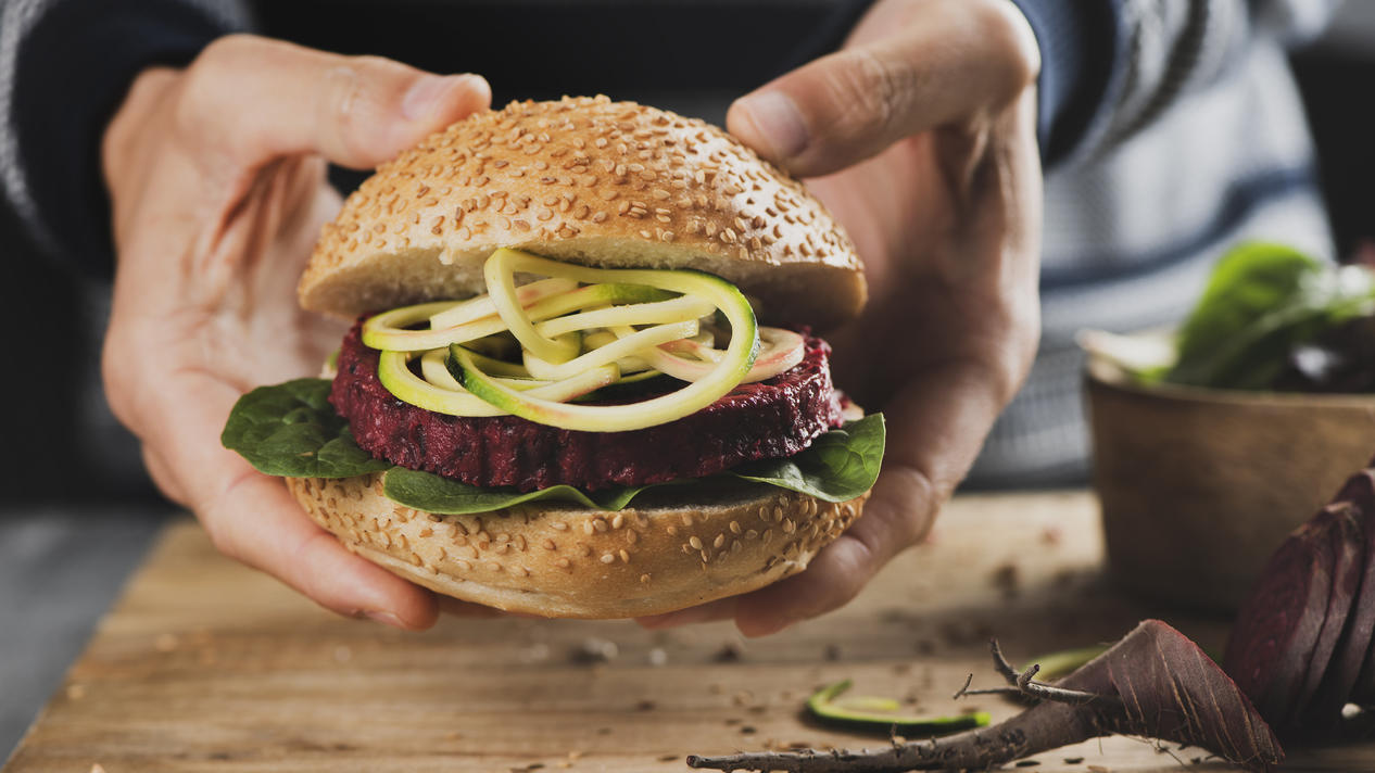 Veggie-Burger-Patties im Test: Diese bekannte Marke fällt durch Ein junger Mann hält einen appetitlichen Veggie-Burger in der Hand