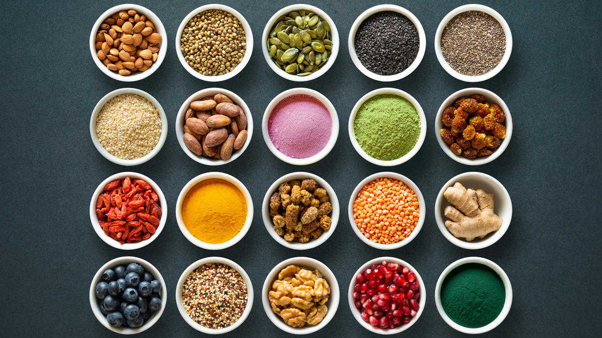Chia-Samen, Kurkuma & Co.: Welches Superfood kann was? Verschiedene Superfoods in kleinen Gläsern, zum Beispiel Matcha, Spirulina, Quinoa, Goji-Beeren