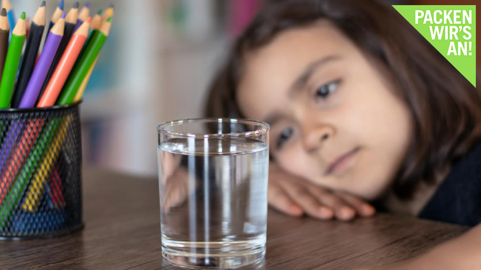 Kleines Mädchen betrachtet nachdenklich ein Wasserglas