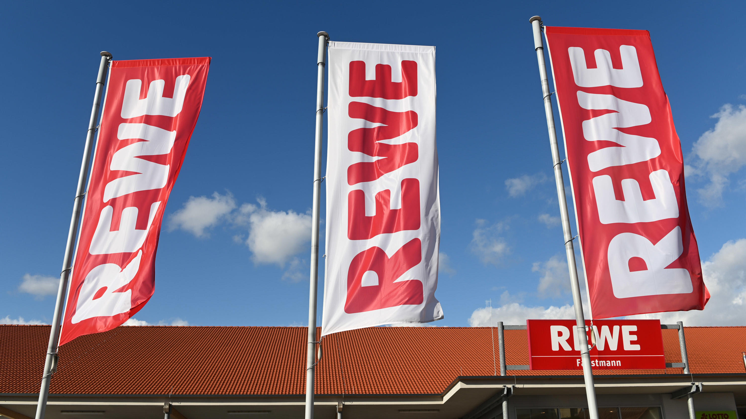 Aufgepasst! Beliebtes TK-Produkt bei Rewe zurückgerufen ARCHIV - 25.02.2020, Hessen, Volkmarsen: Fahnen mit dem Logo des Lebensmitteleinzelhändlers Rewe wehen vor einer Filiale. Ein Ende der Preiserhöhungen im deutschen Lebensmittelhandel ist nach Einschätzung von Rewe-Chef Souque nicht in Sicht. (zu dpa