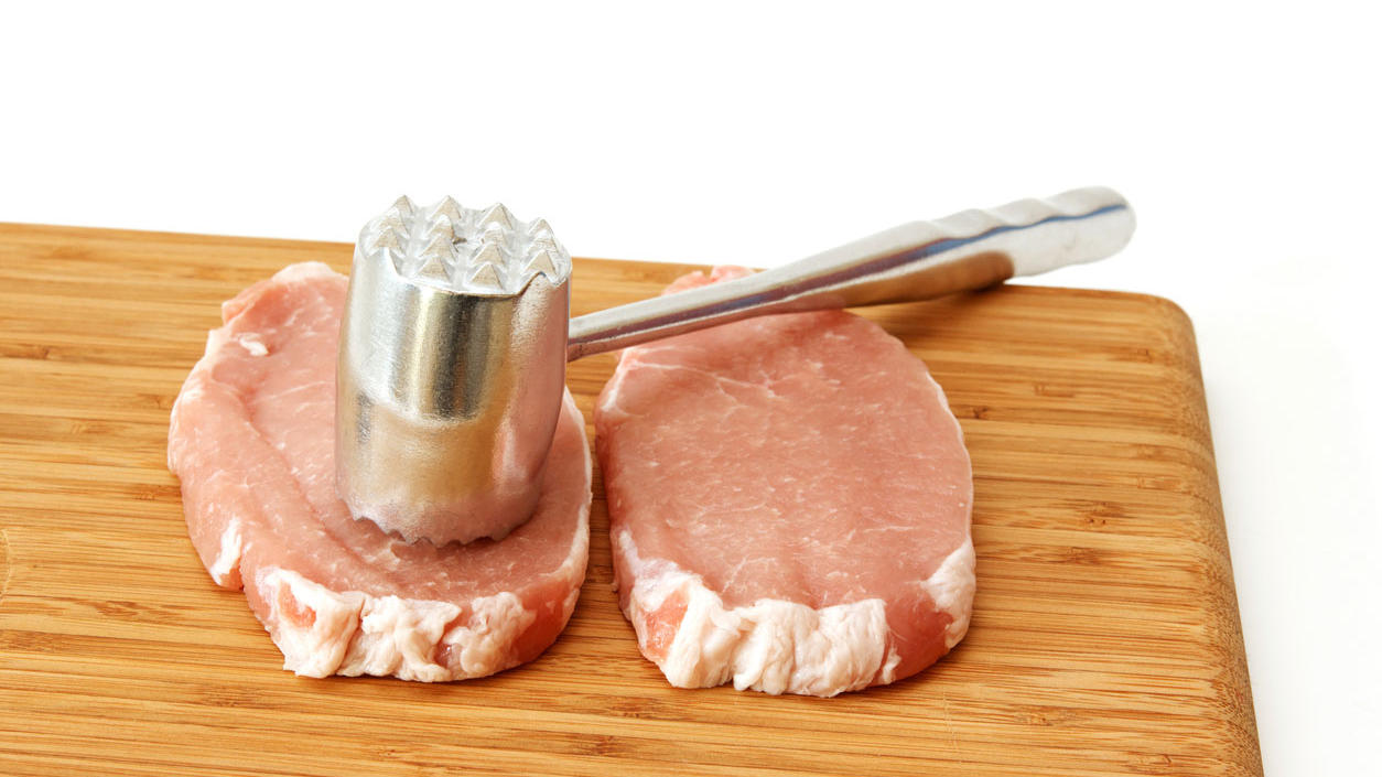 Fleischklopfer – mit sanftem Hämmern zum perfekten Fleischgenuss Ein Fleischklopfer und zwei Stück Fleisch liegen auf einem Holzbrett.