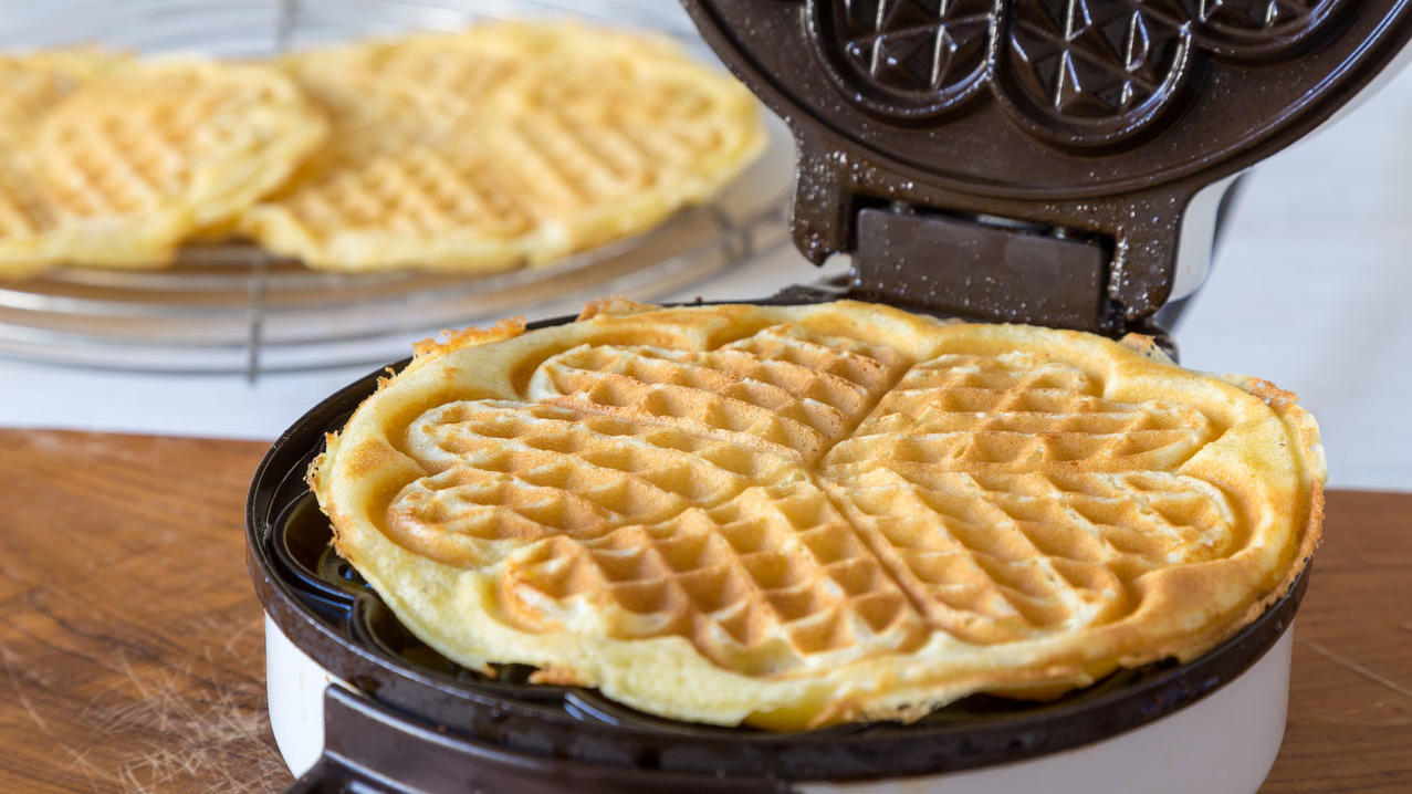 Belgische und bergische Waffeln mit Puderzucker, Sahne und Kirschen Herzwaffel in einem Waffeleisen