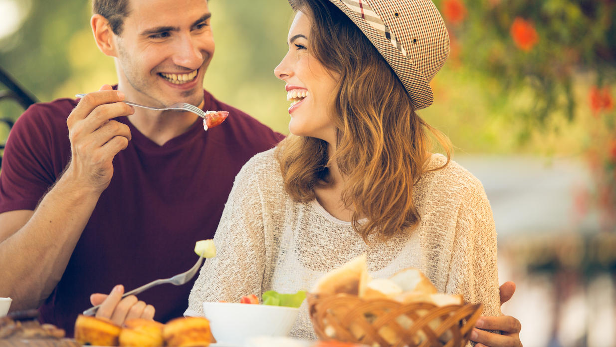 So verändert sich das Essverhalten beim Date mit einem attraktiven Partner Couple enjoying lunch at a restaurant, holding hands, looking away.