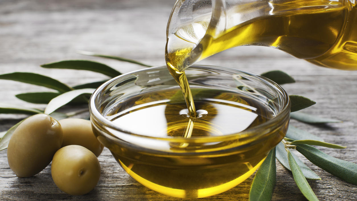 Aus einer Karaffe wird Olivenöl in eine Schüssel gegossen.